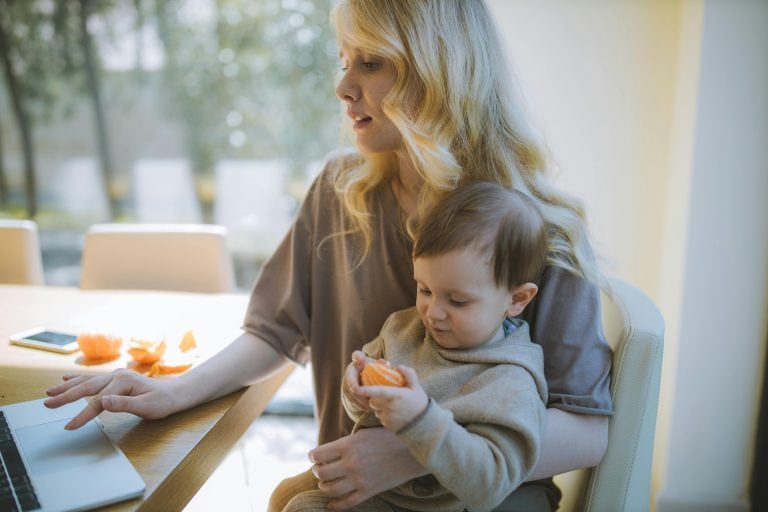 Femme tenant bébé sur les genoux, travaillant sur ordinateur