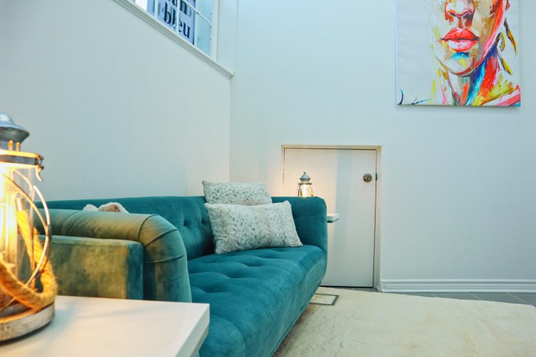 Le bureau de thérapie de Jenny est décoré d'un canapé turquoise, de lampes de table au style rustique, et d'une peinture vibrante et multicolore représentant un visage, accrochée au mur.