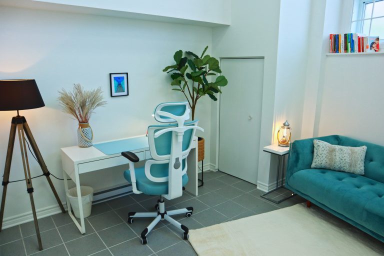 On aperçoit le bureau et la chaise de la thérapeute ainsi qu'un coin du canapé. Tout est dans une palette de blanc et de bleu avec des éléments naturels pour créer une atmosphère calme.