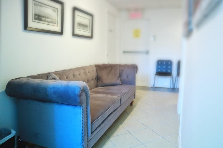 La salle d'attente que vous verrez en arrivant. Un canapé gris dans un couloir avec des cadres photo simples accrochés au-dessus.