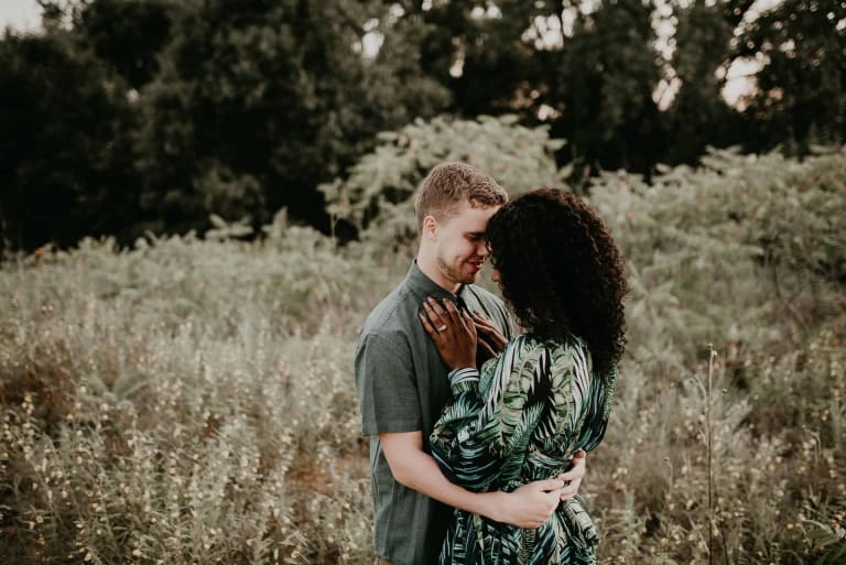 A couple stands in each others arms in a field, a look of love in their eyes