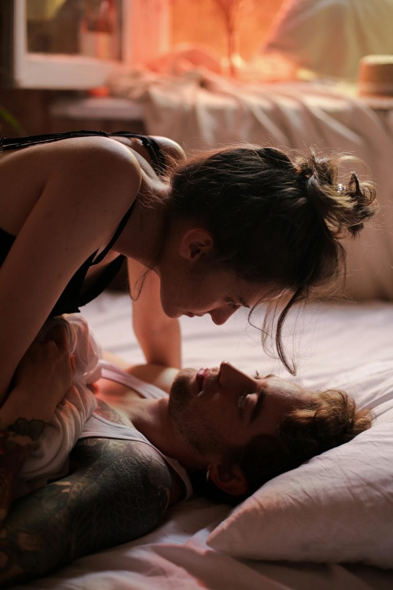 Un couple allongé sur un lit se regarde tendrement dans les yeux.