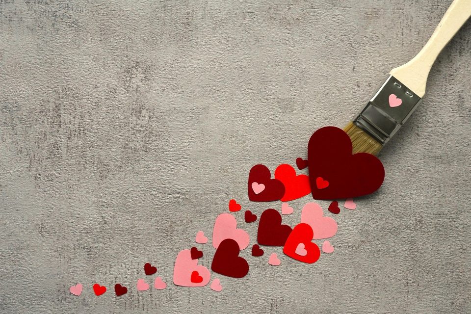 A paint brush leaving behind a trail of cut out paper hearts.