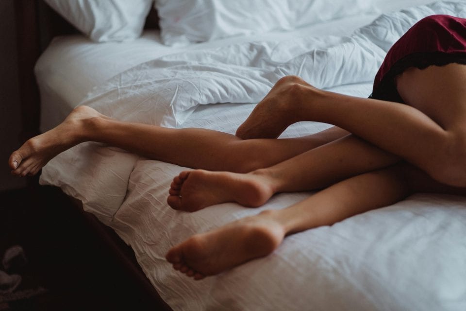 Deux paires de jambes dans un lit.
