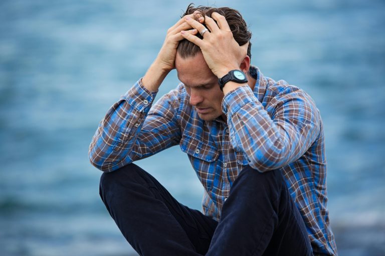 a man sitting on the beach and holding his head in distress